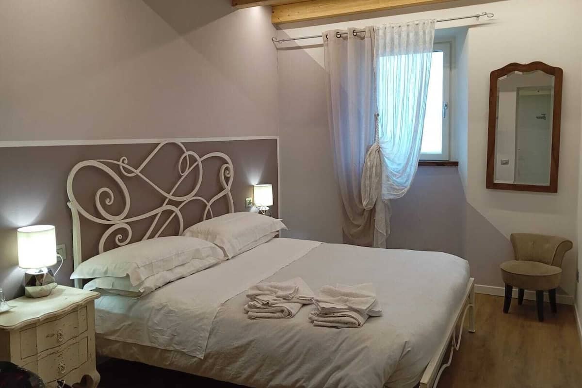 A bedroom with a bed, bedside lamps, a chair, a mirror, and a window with curtains.