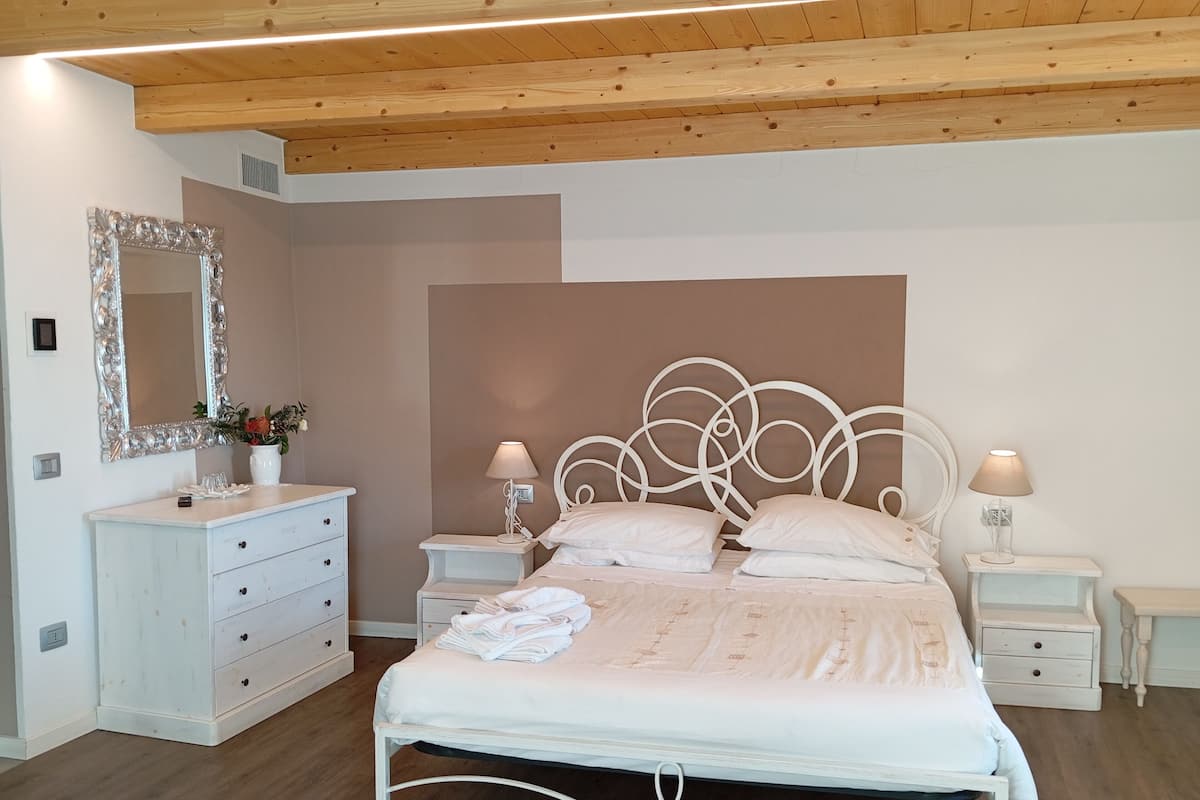 A bedroom with a white metal bed frame, a white dresser, two bedside tables with lamps, and a large mirror on the wall.