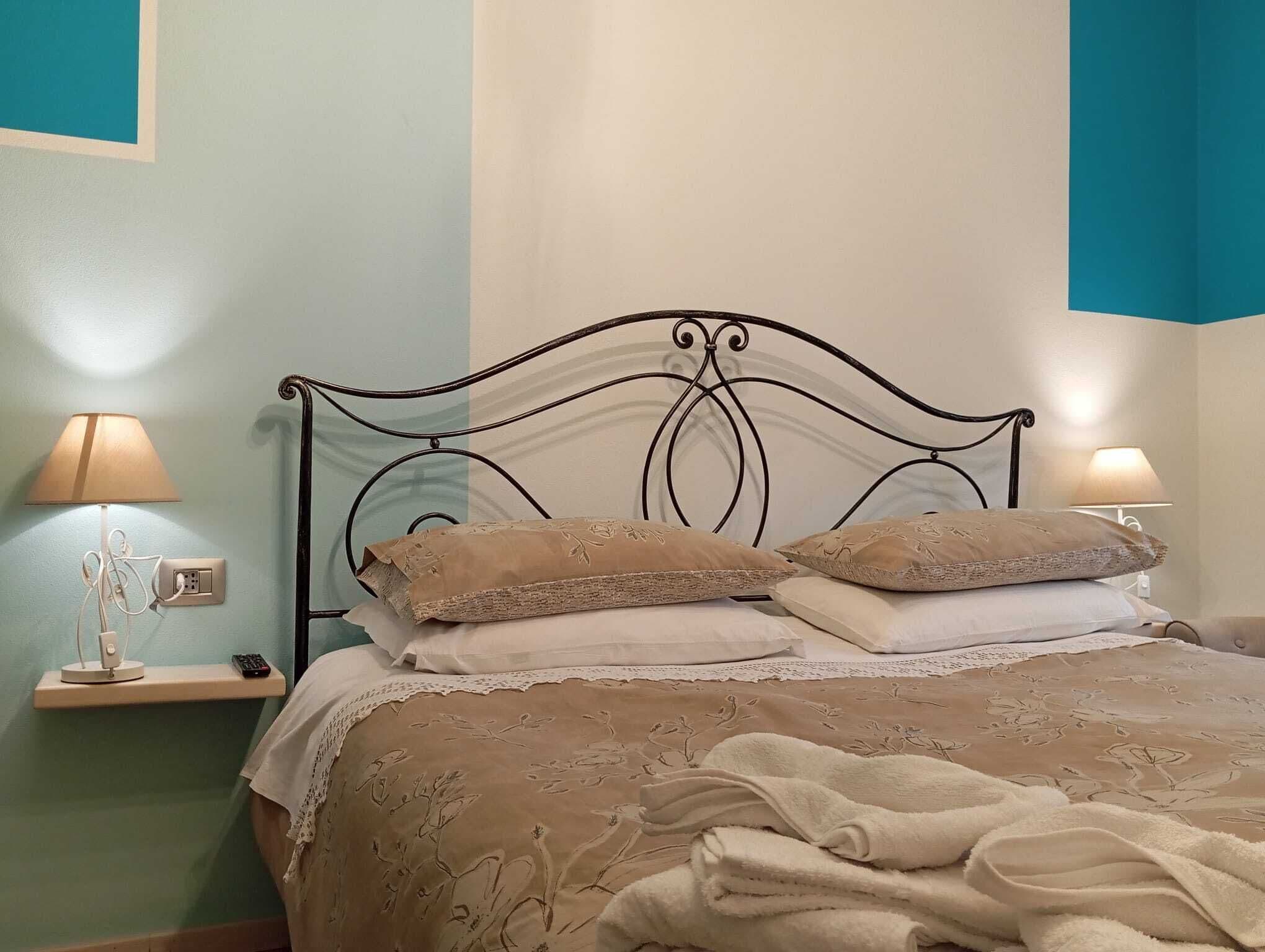 A neatly made bed with a patterned bedspread and two decorative pillows, flanked by bedside tables with lamps and a power outlet.