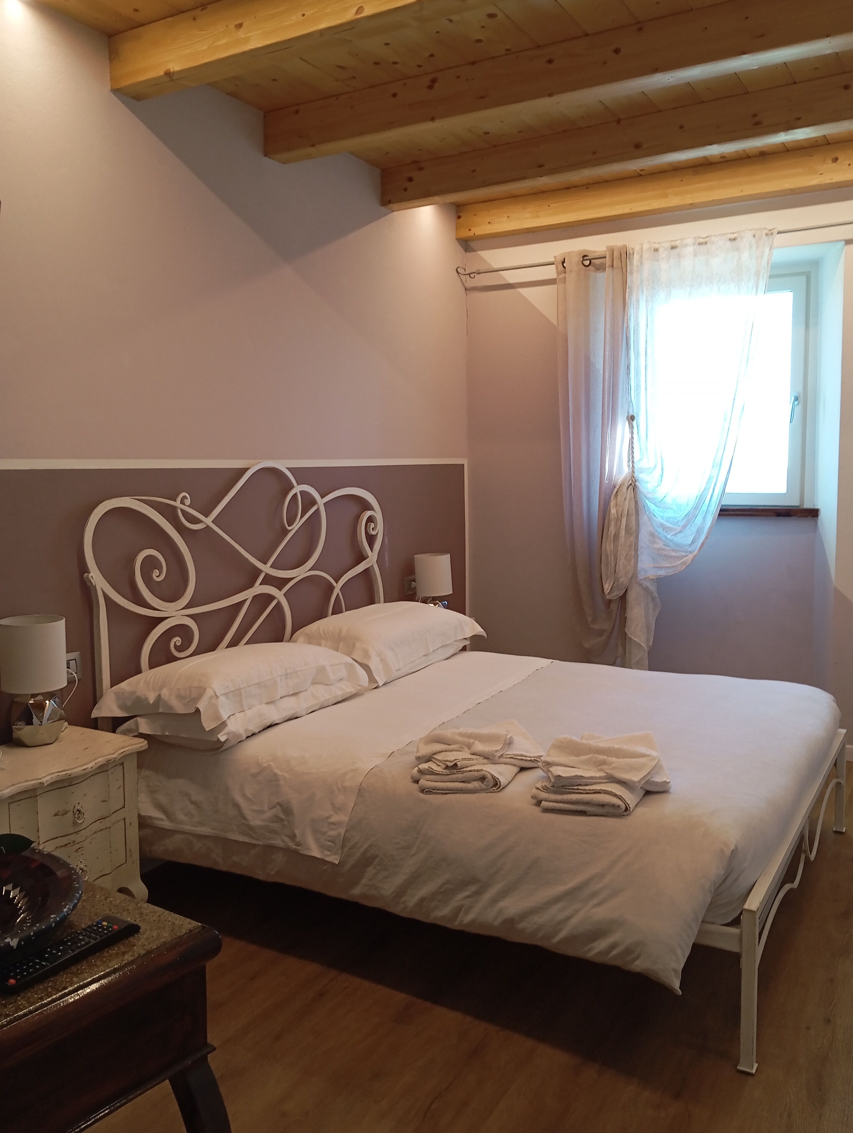 A bedroom with a bed, bedside table, lamp, and window with curtains.