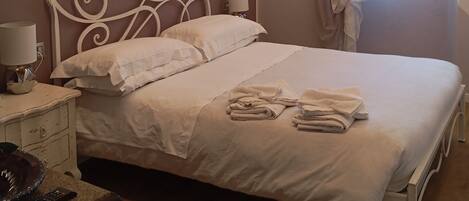 Un dormitorio con cama, mesita de noche, lámpara y ventana con cortinas.