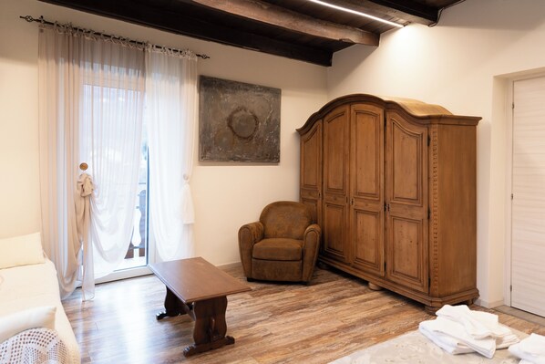 A room with a wooden floor, a large wooden cabinet, a brown armchair, a wooden table, and a white door. - Roncola B&B L'Antica Corte (Roncola)