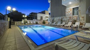 A swimming pool with lounge chairs and a building with a stone facade. - Mandy Suites (Kissamos)
