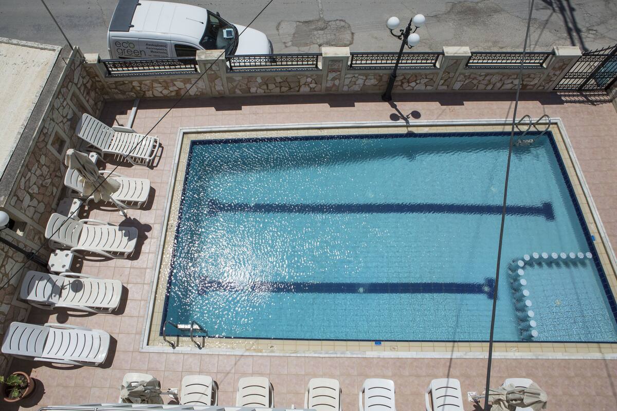 A rectangular swimming pool with clear blue water, surrounded by white lounge chairs and a stone wall.