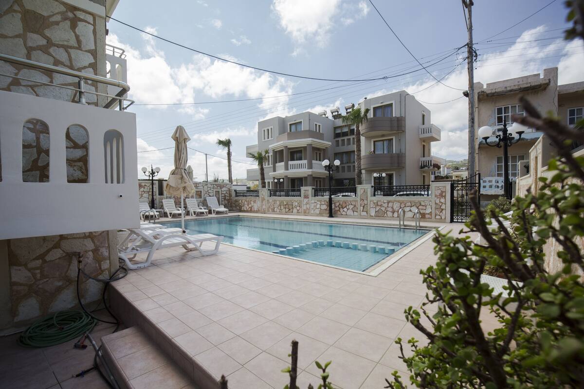 A swimming pool with lounge chairs, a stone wall, and a multi-story building in the background.