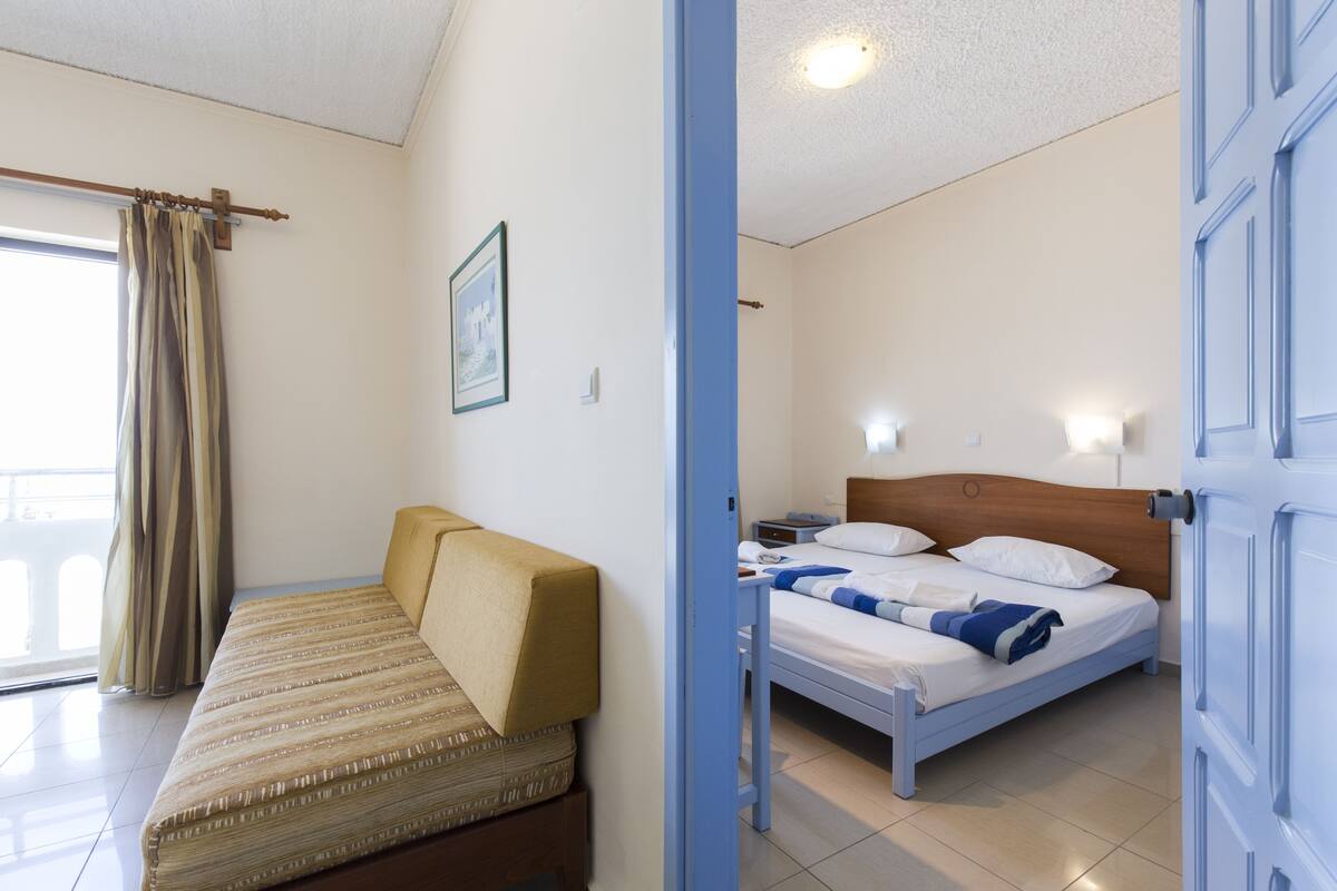 A room with a bed, a sofa, a window with curtains, and a door.