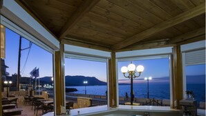 An outdoor seating area with tables and chairs, overlooking a body of water and a distant mountain range. - Mandy Suites (Kissamos)