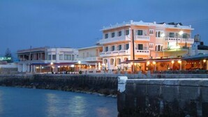 A waterfront hotel with multiple stories, balconies, and outdoor seating areas. - Mandy Suites (Kissamos)