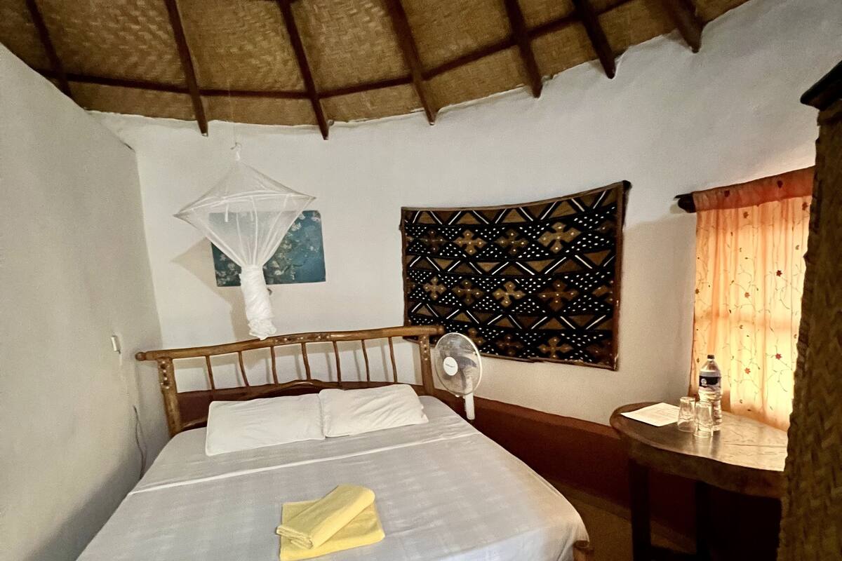 A room with a bed, a table, a chair, a wall hanging, and a mosquito net.