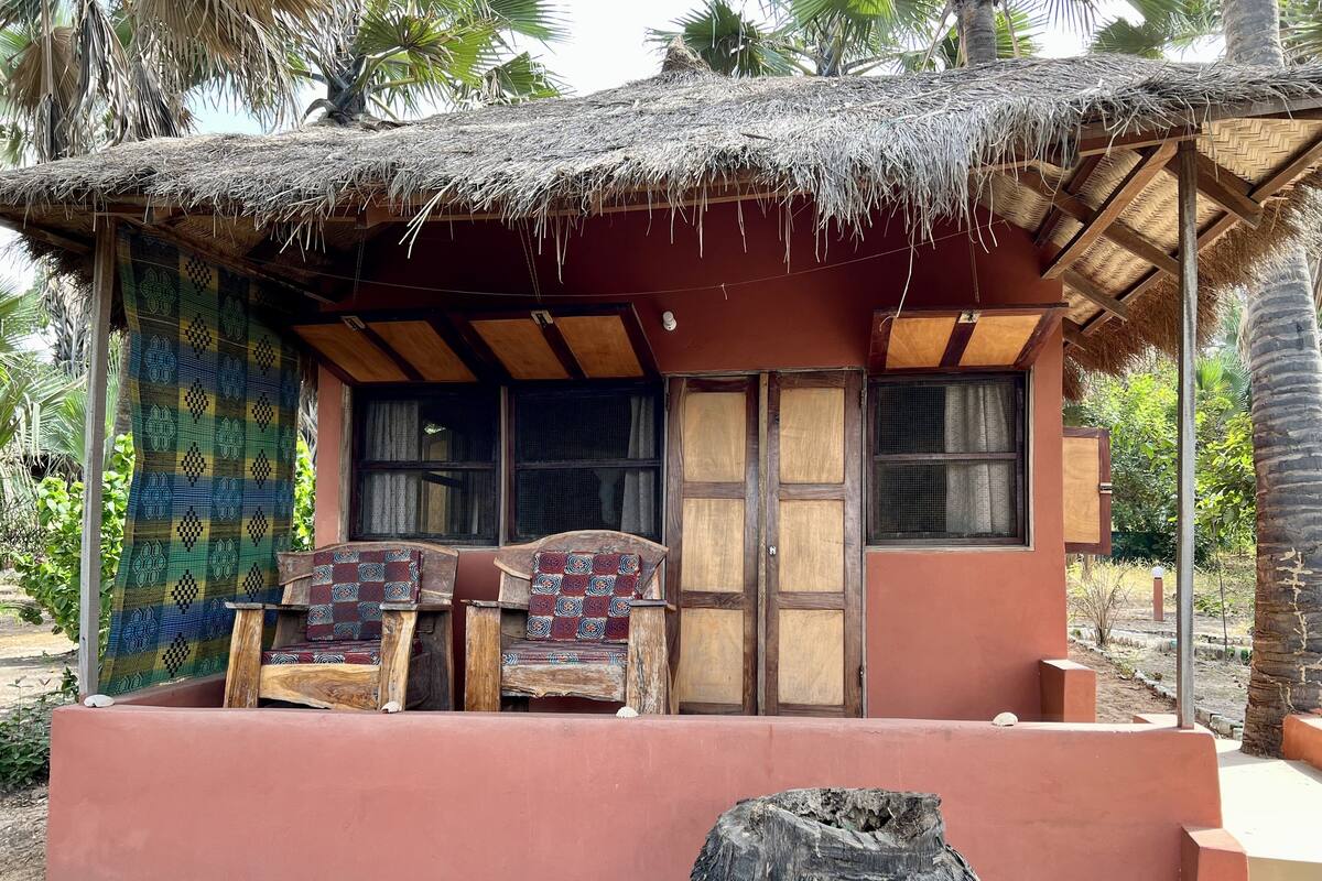 A thatched-roof hut with two wooden-framed windows and a bench with patterned cushions.