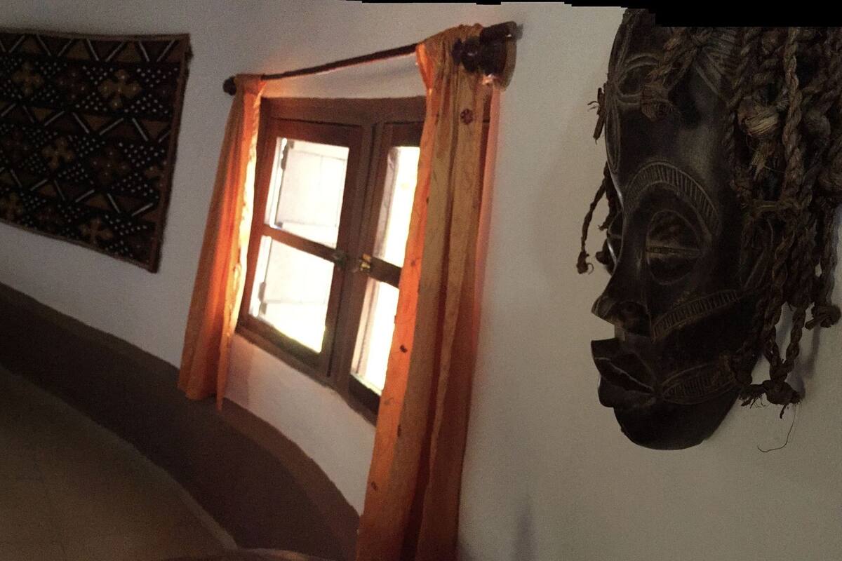 A bedroom with a wooden bed, a window with curtains, a wall-mounted tapestry, and a small staircase leading to another room.