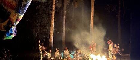 A group of people around a campfire in a forested area at night.