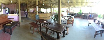 Un restaurante rústico con mesas y bancos de madera, una zona de bar y un techo de paja.