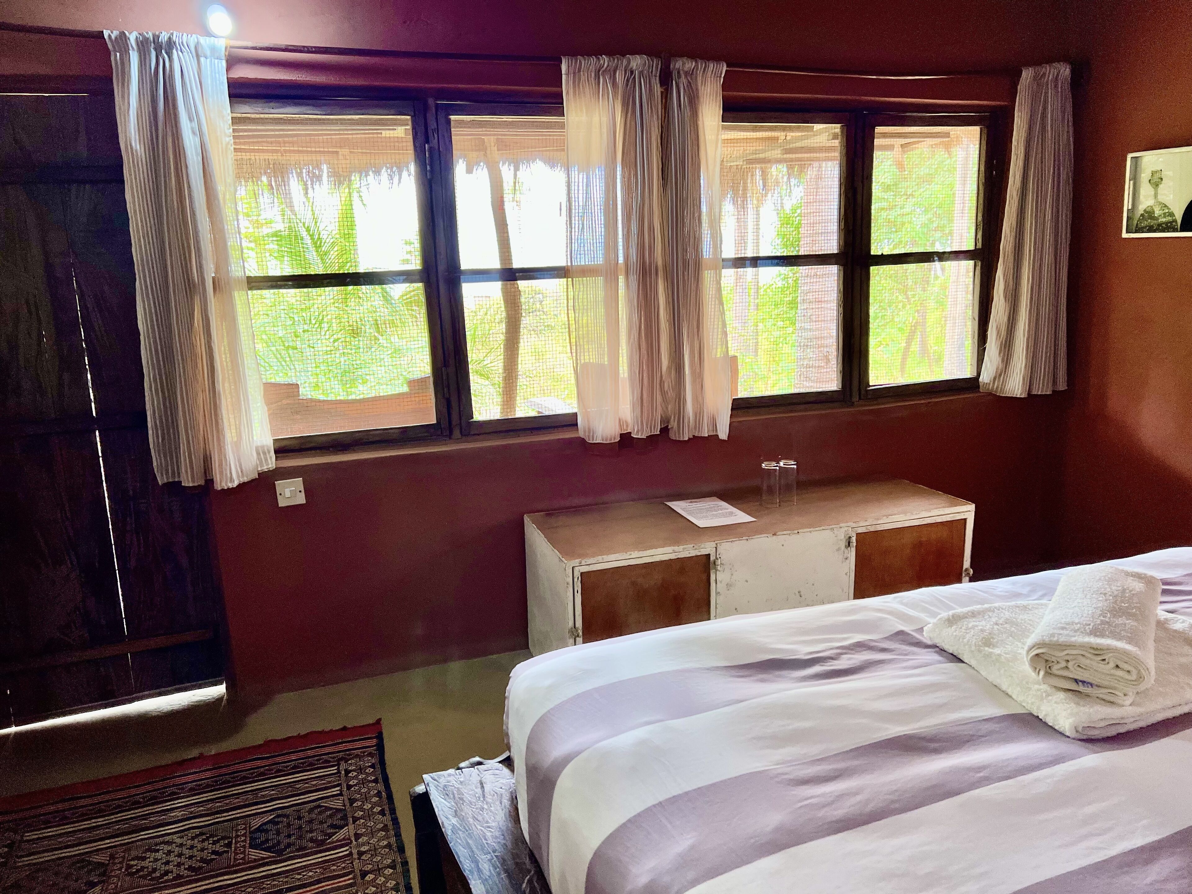 A room with a bed, a small wooden cabinet, and a window with curtains.