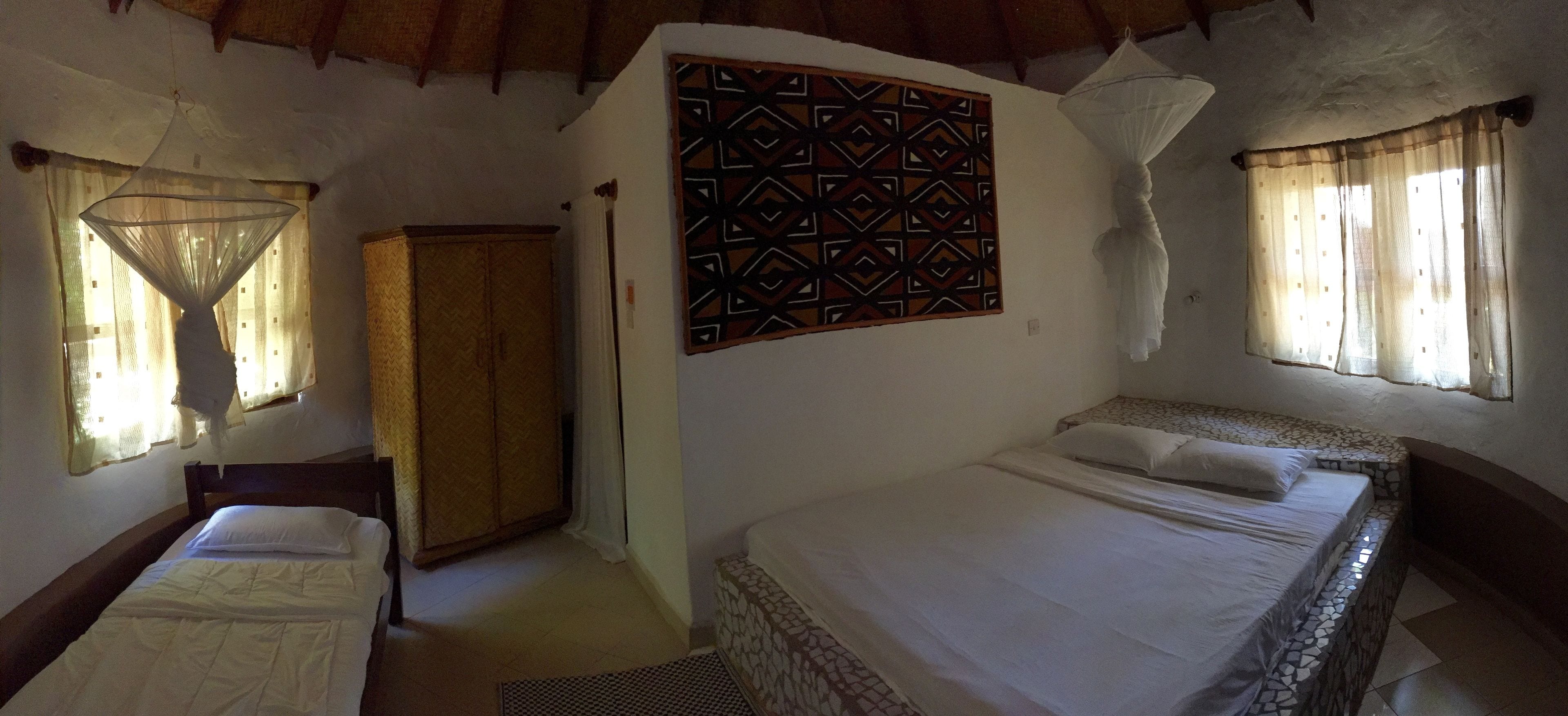 A room with two beds, a wardrobe, a decorative wall hanging, and a mosquito net.