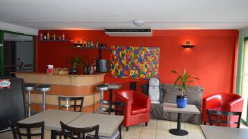 Un restaurante con paredes rojas, un cuadro abstracto de colores y una zona de bar con taburetes.