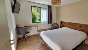 Ett sovrum med en säng, ett skrivbord, en stol, en tv och ett fönster med gardiner.