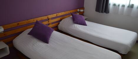Two single beds with wooden headboards and white bedding, a nightstand, and a window with curtains.