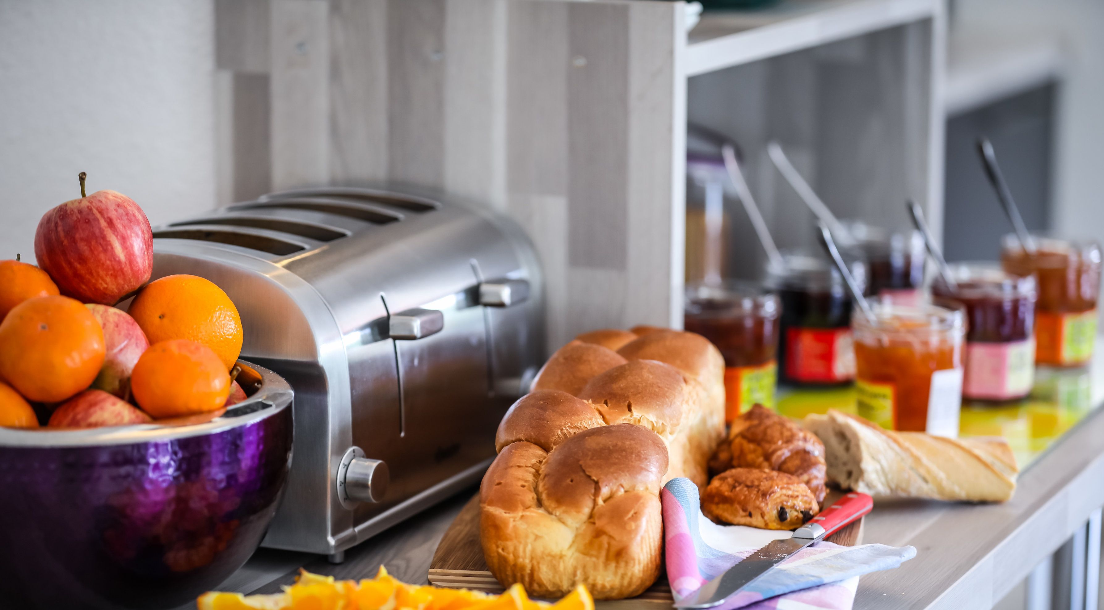 A breakfast buffet with a toaster, fruits, pastries, and condiments.