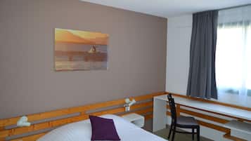 A hotel room with a bed, a desk, a chair, a window with curtains, and a painting on the wall.