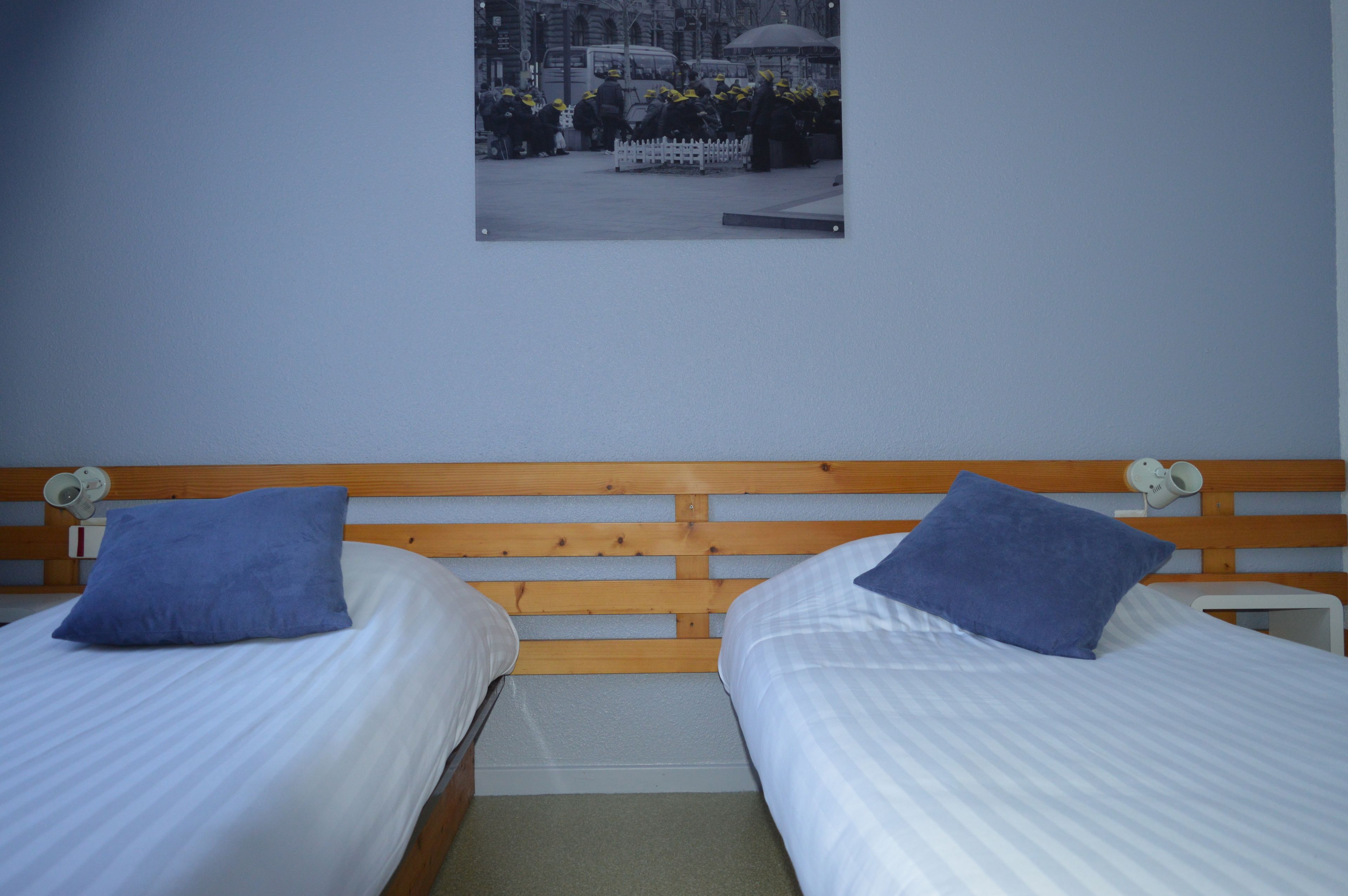 A bedroom with two beds, each with a blue pillow and white bedding.