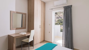 A bedroom with a wooden desk, a chair, a bed, a window with curtains, and an air conditioning unit. - Matala Bay Apartments (Faistos)