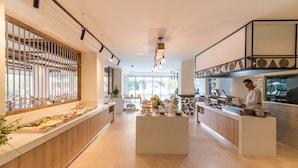 A modern kitchen with a central island, wooden accents, and a large window with a view. - Matala Bay Apartments (Faistos)
