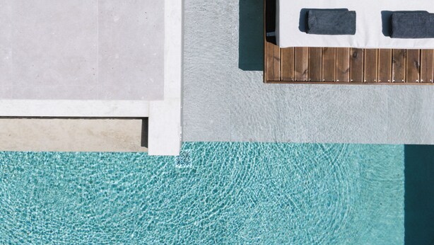 A poolside bed with a wooden frame, white bedding, and two pillows. - Matala Bay Apartments (Faistos)
