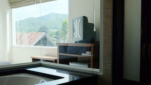 Une salle de bain avec une baignoire, un téléviseur posé sur un meuble en bois et une fenêtre donnant sur les montagnes.