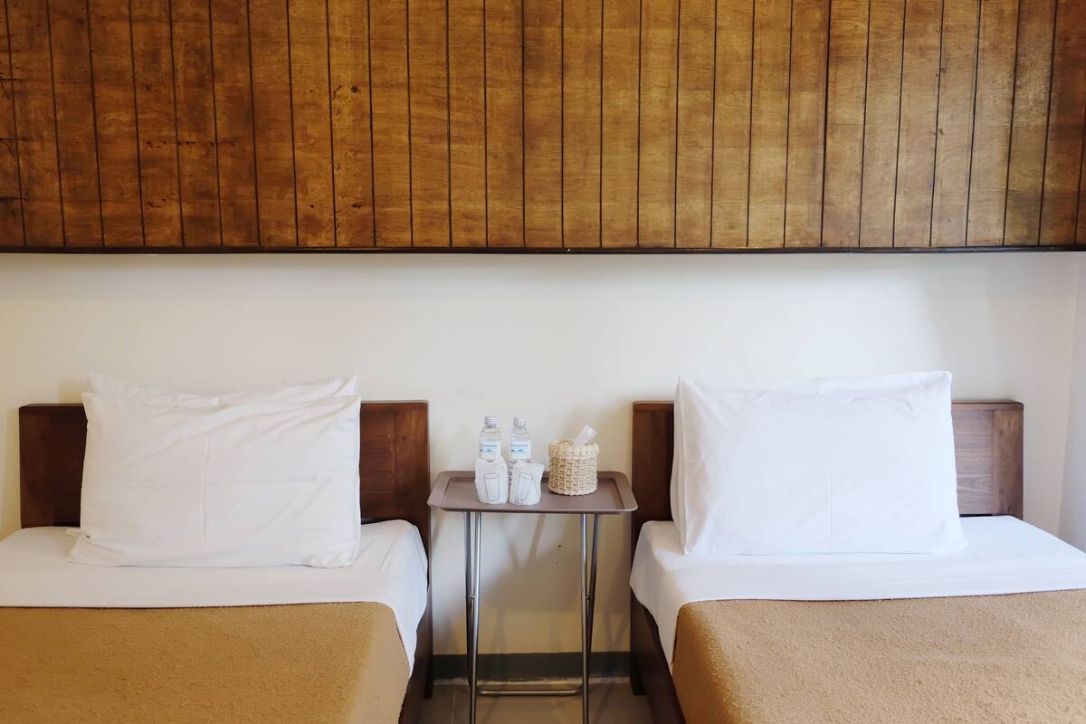 A hotel room with two beds, a small table with toiletries, and a wooden headboard.