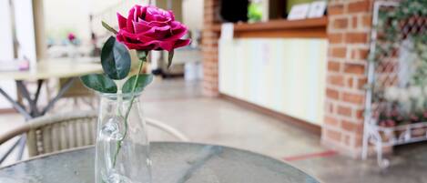 Un vase en verre contenant une fleur rose, posé sur une table ronde dans un cadre extérieur.