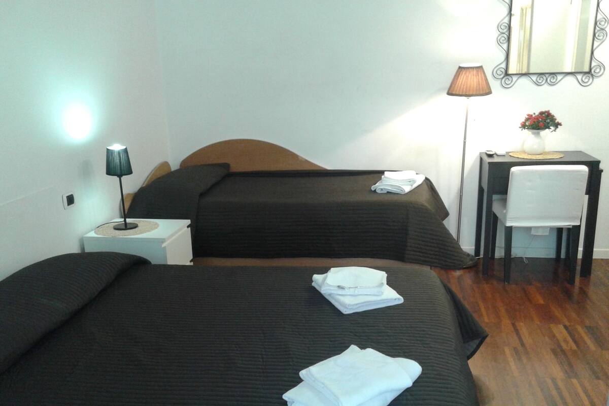 Una habitación de hotel con dos camas, un escritorio, una silla, una lámpara y un espejo.