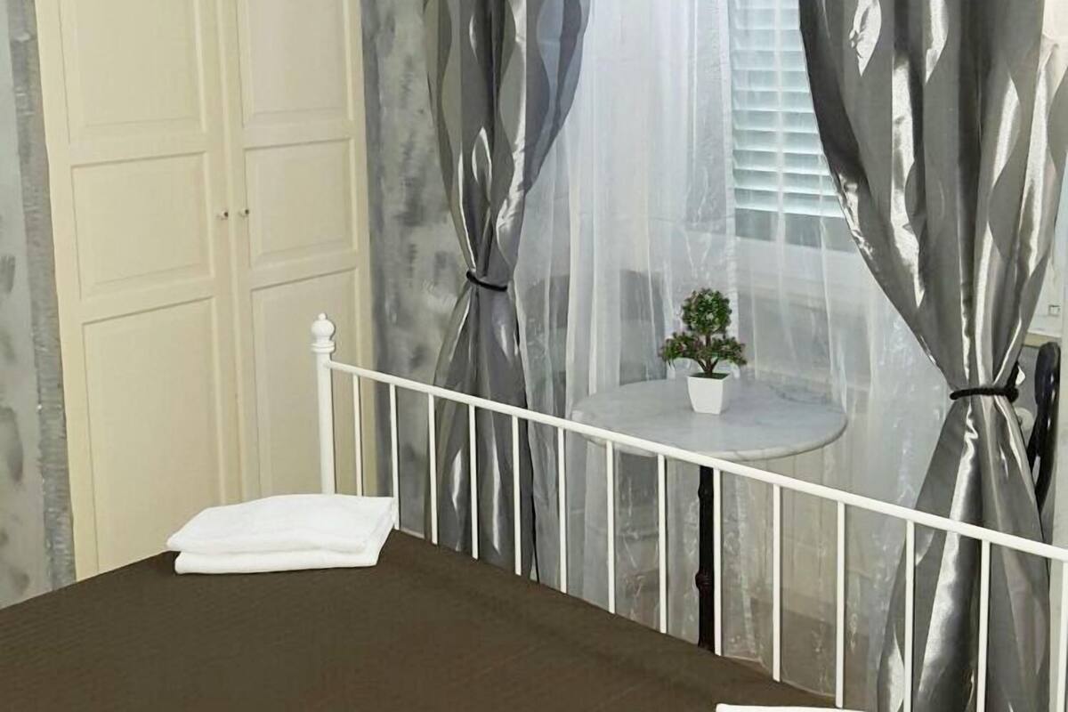 Un dormitorio con cama, una mesita con una planta y cortinas.