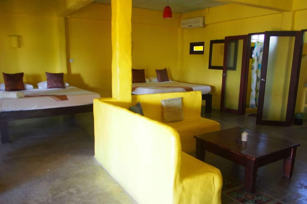 Een kamer met gele wanden, een bank, een bed, een houten tafel en een spiegel.