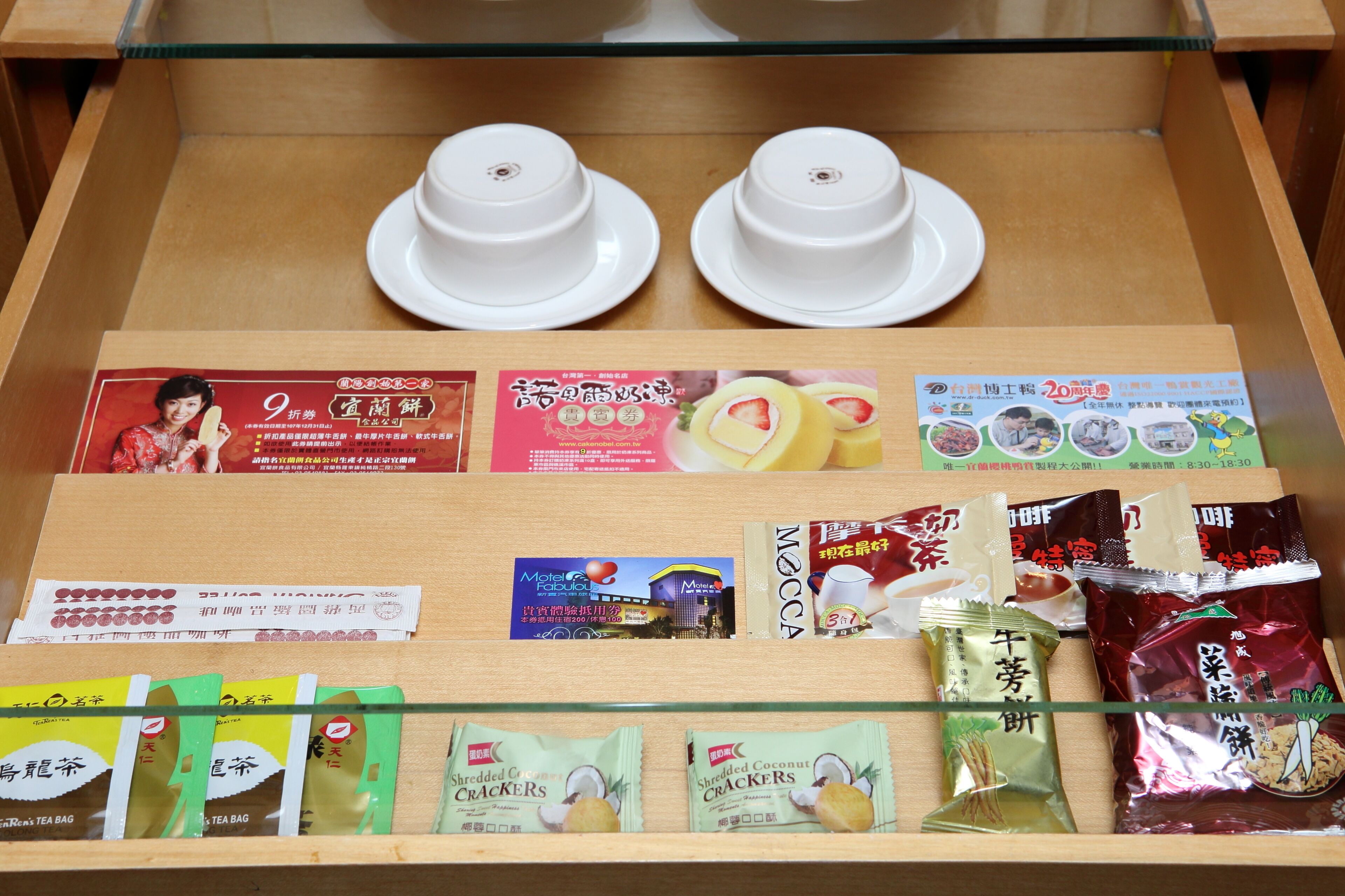 Vitrine com duas xícaras de chá brancas, embalagens de diversos petiscos e material promocional.