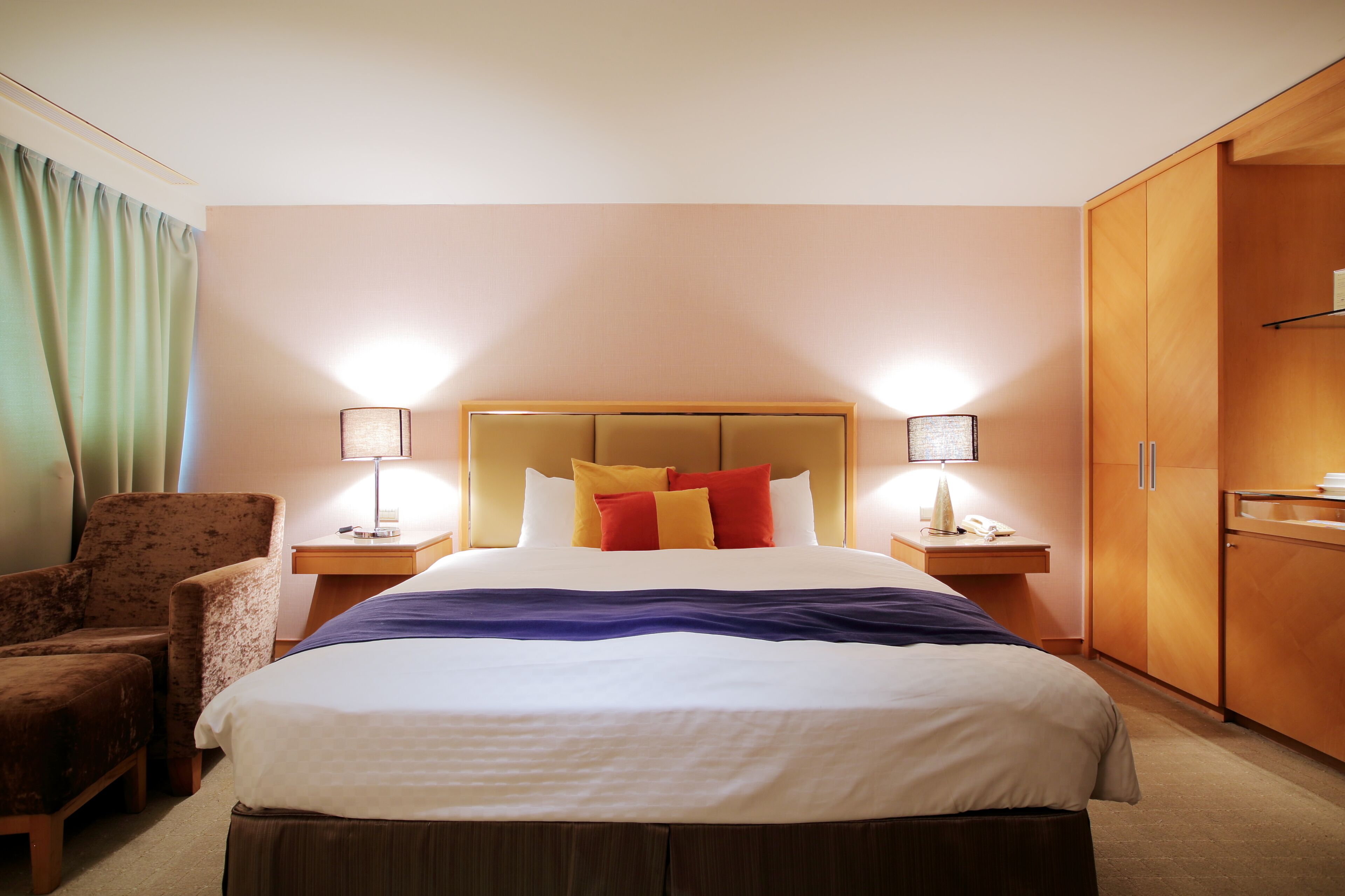 Una habitación de hotel con una cama grande, dos lámparas de noche, un armario de madera y una silla.
