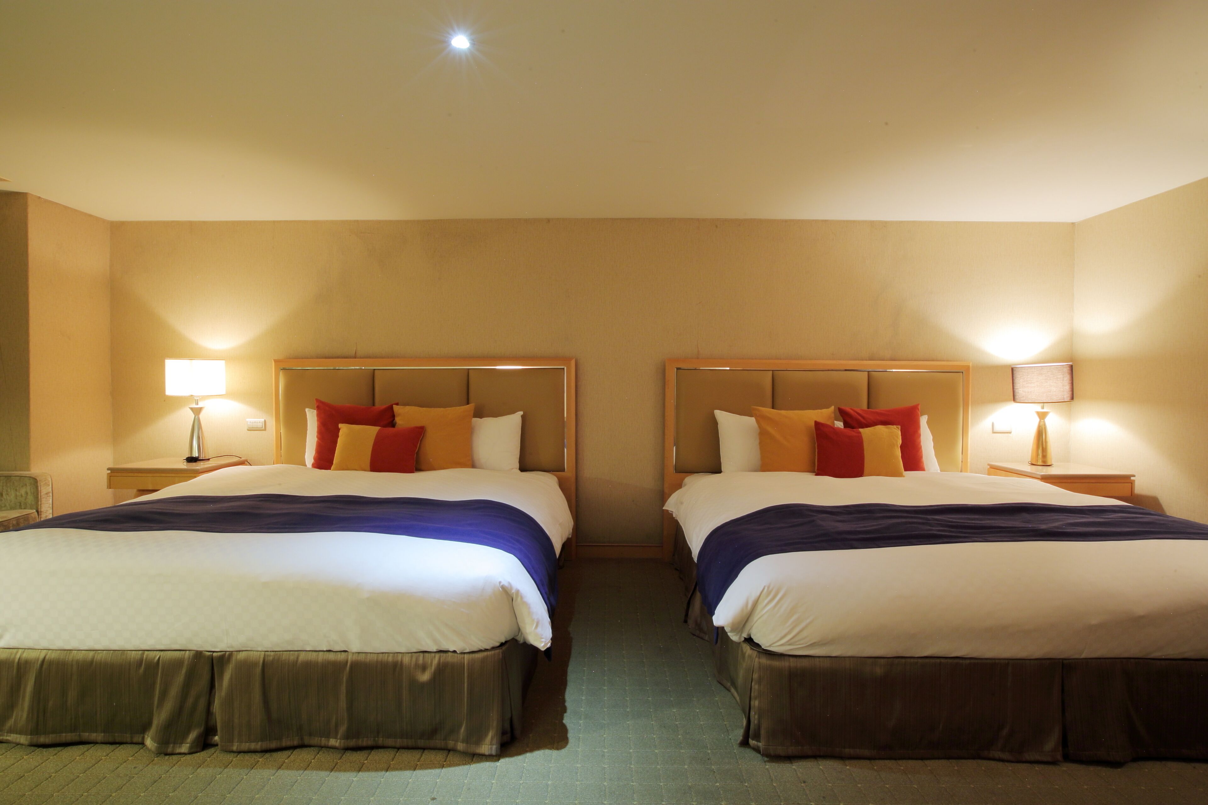 A hotel room with two beds, each with a headboard, bedside tables, and lamps.