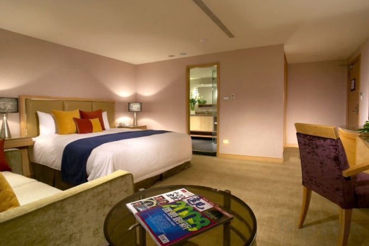 Une chambre d’hôtel avec un lit, un bureau, une chaise et une petite table ronde sur laquelle se trouve un magazine.