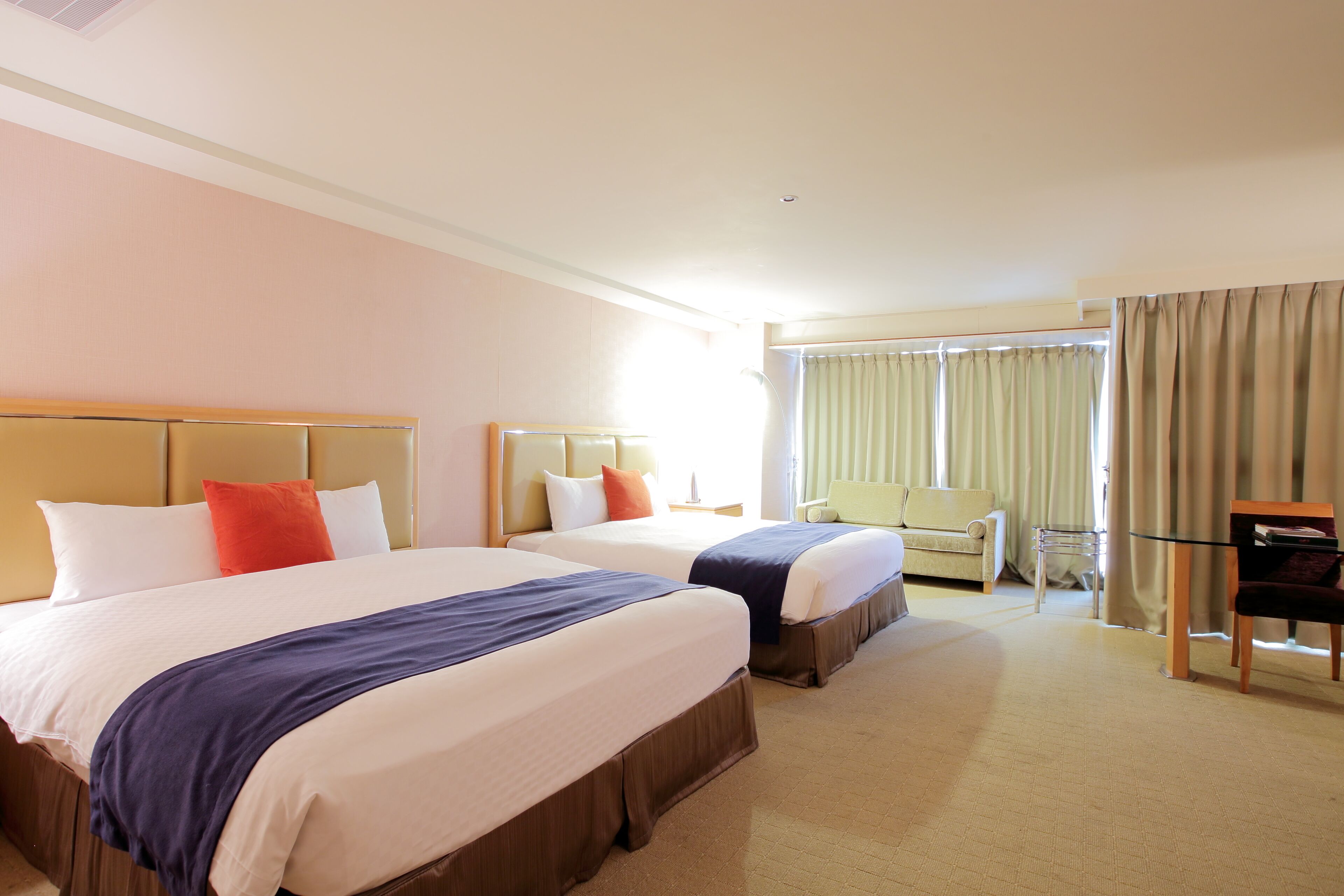 Habitación de hotel con dos camas, una silla, un escritorio y un ventanal grande con cortinas.