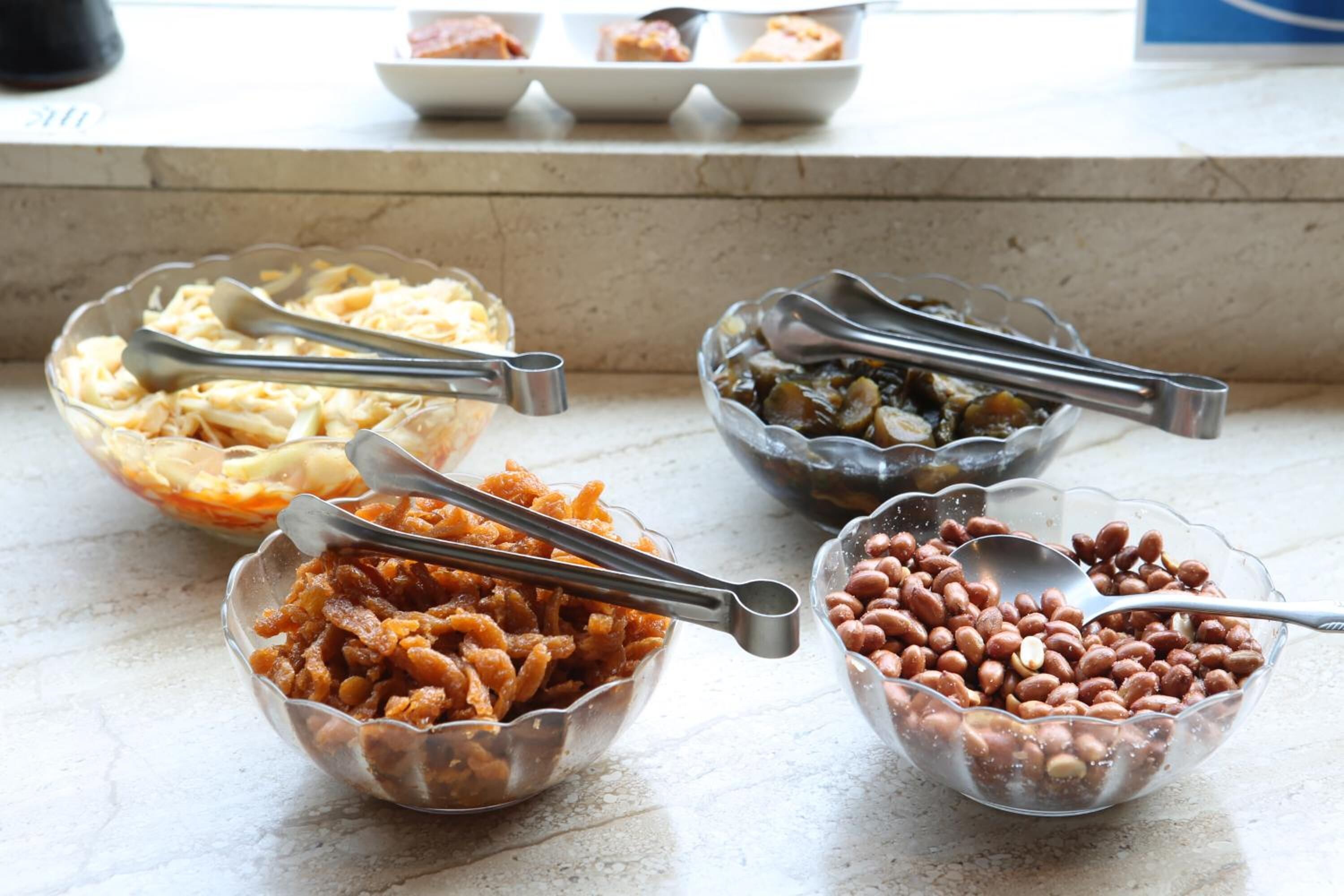 Four glass bowls with metal tongs on a marble countertop.