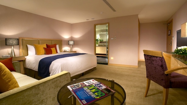 Une chambre d’hôtel comprenant un lit, des tables de chevet, un bureau, une chaise et une table ronde avec un magazine.