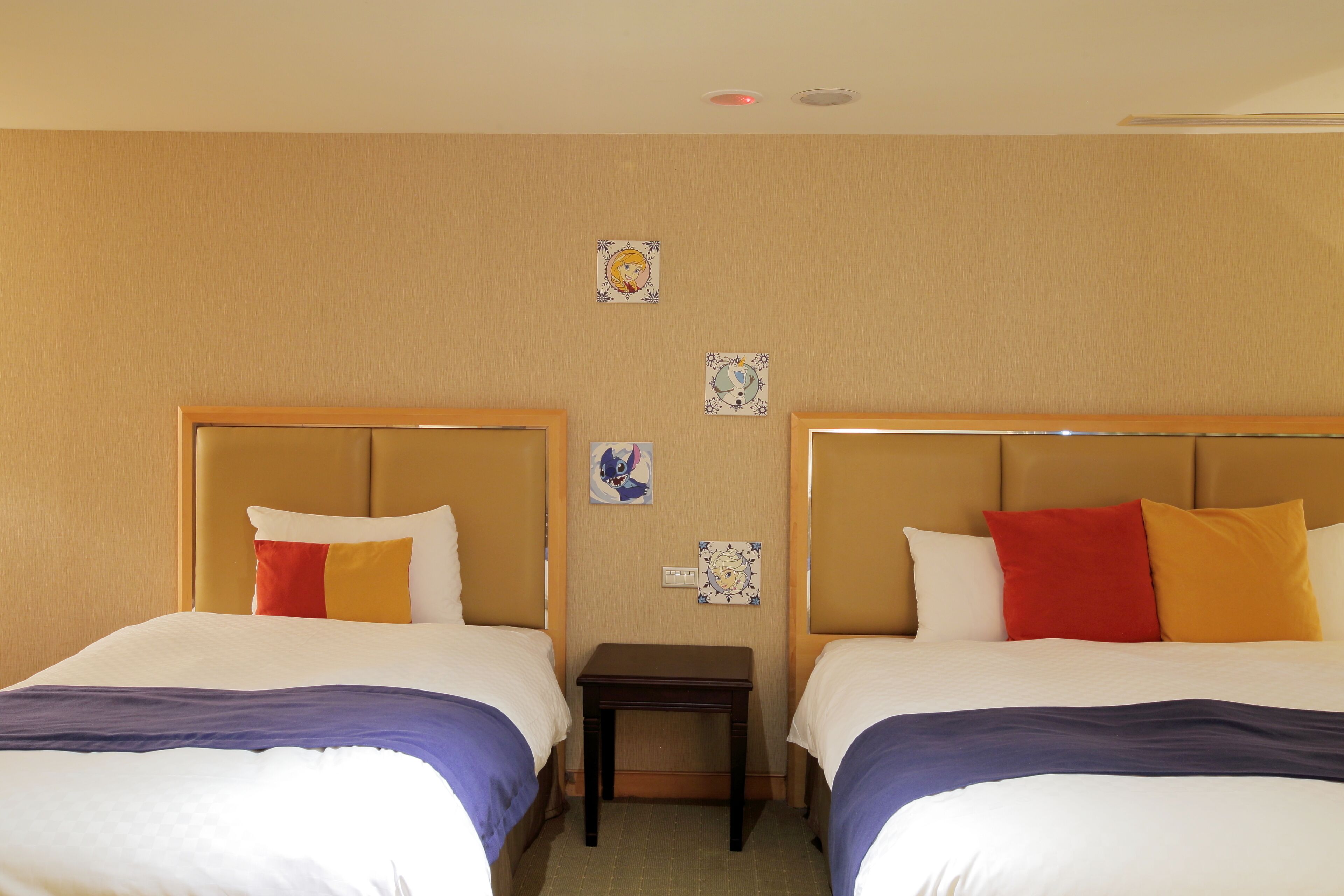 A hotel room with two beds, each with a headboard, a small bedside table, and a wall-mounted artwork.