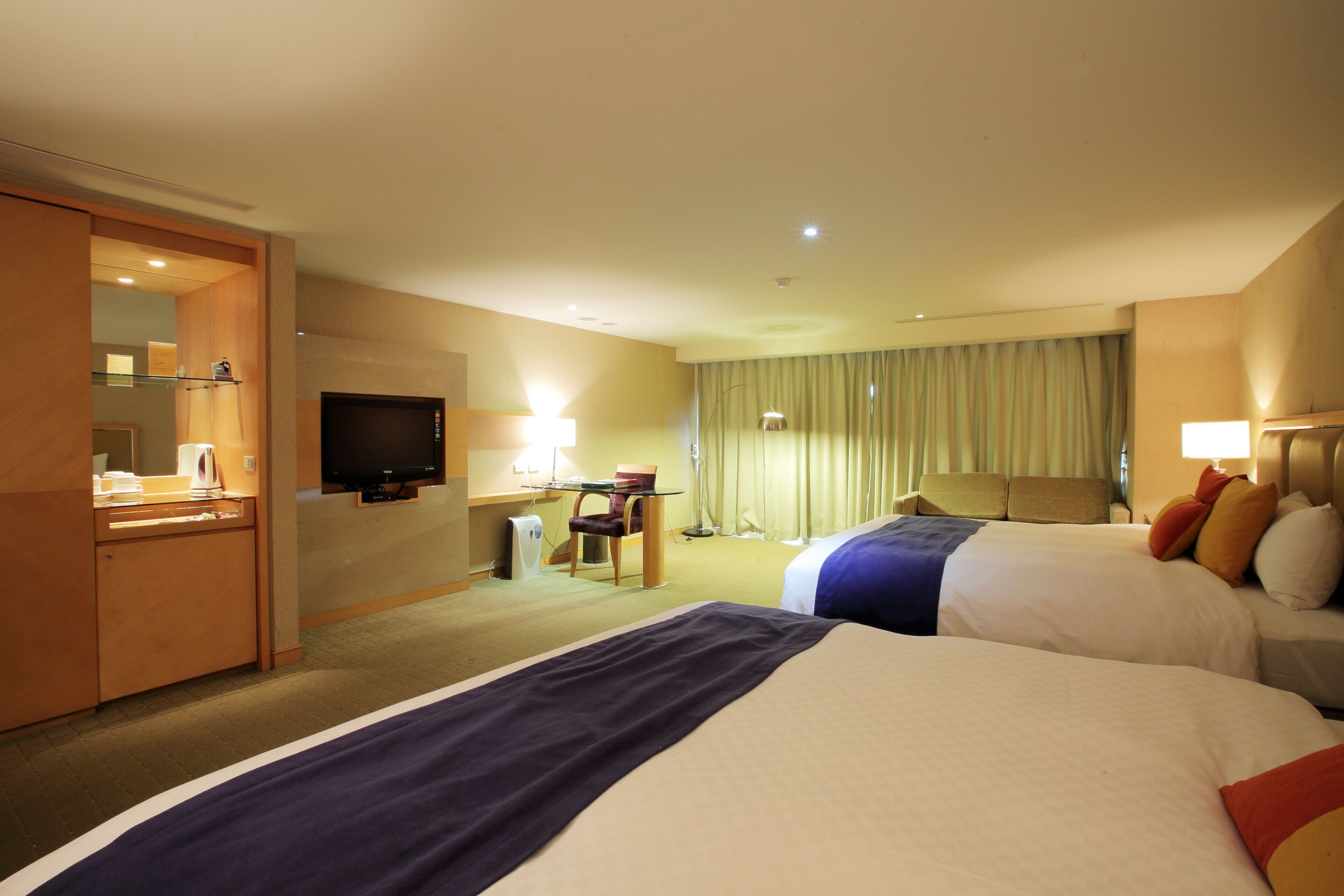 A hotel room with two beds, a desk, a chair, a television, and a bathroom.