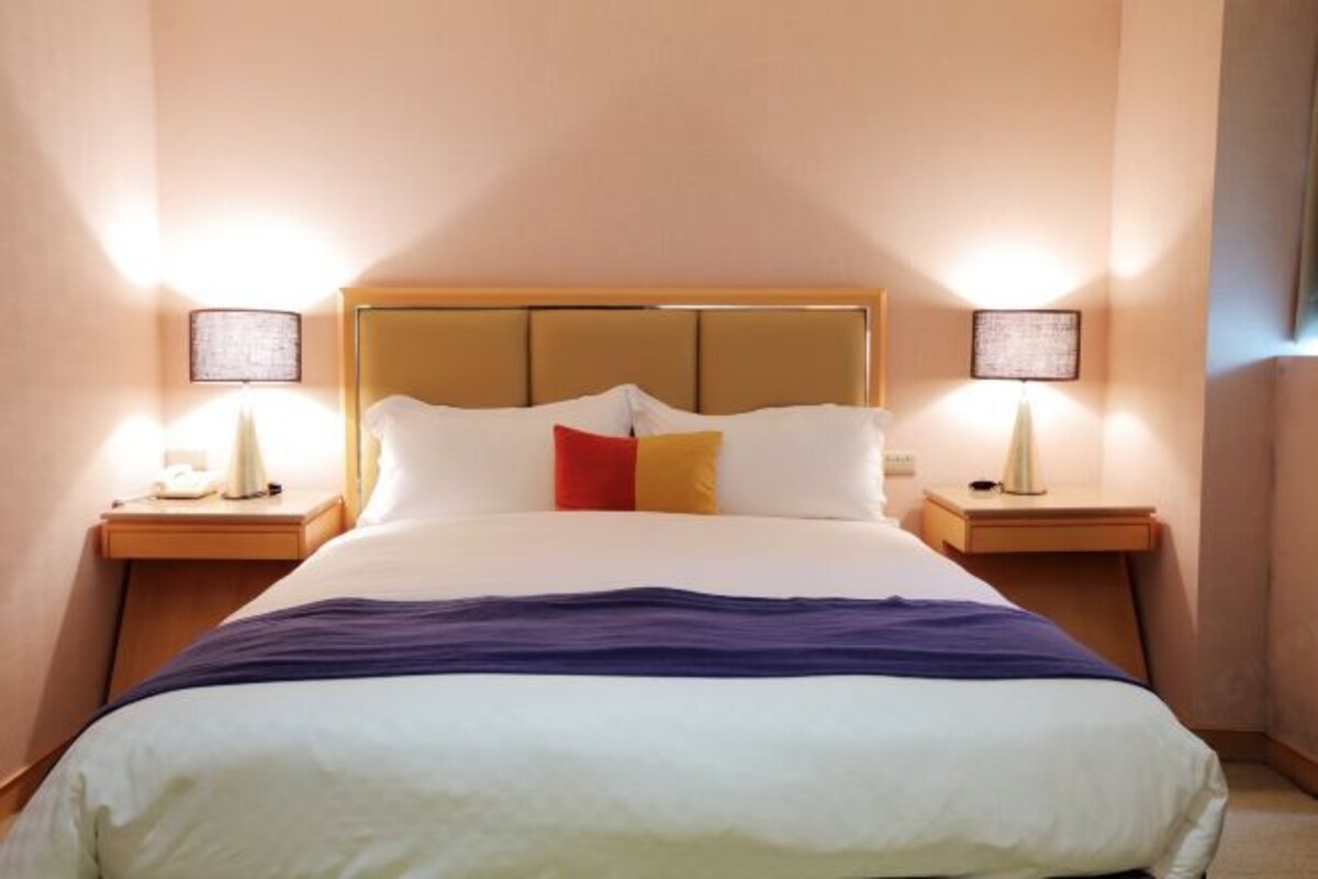 A neatly made bed with a headboard, two bedside tables with lamps, and a wall-mounted light fixture.