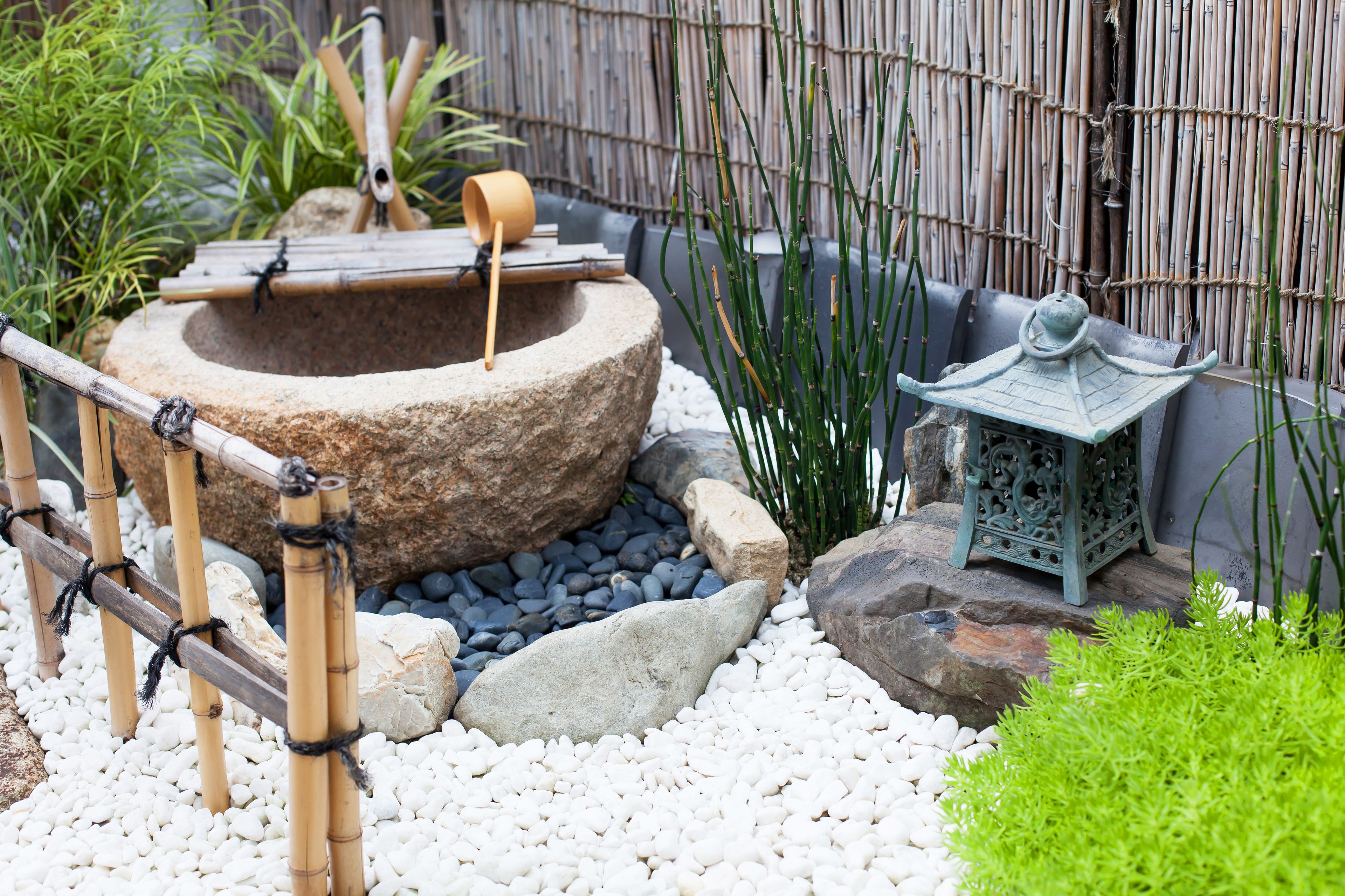 A traditional Japanese garden with a stone basin, bamboo fence, and a lantern.