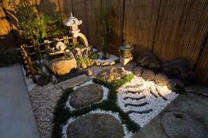 Un jardín con piedras para caminar, una cerca de bambú y faroles tradicionales.