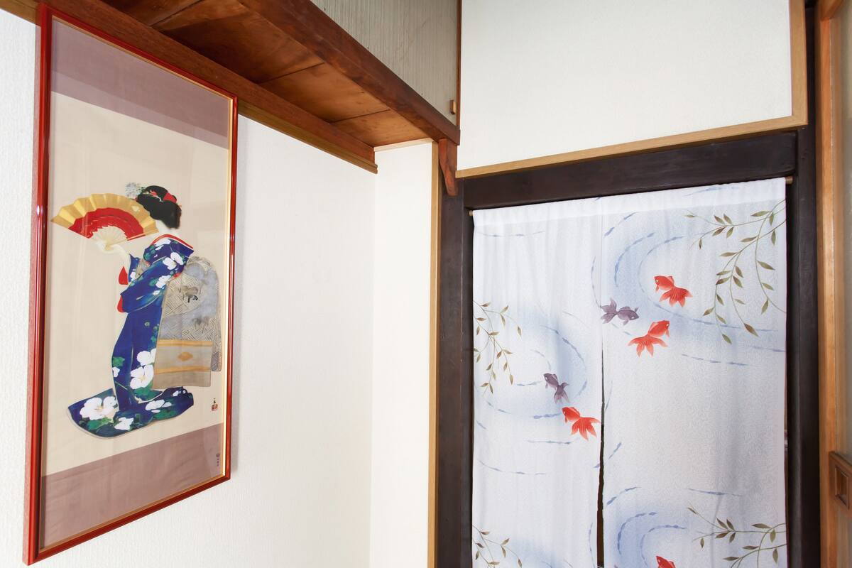 A traditional Japanese room with tatami flooring, a shoji screen, and a framed artwork depicting a kimono.