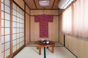 A traditional Japanese room with tatami flooring, a shoji screen, a wooden table with a red kimono, and a ceiling fan. - Kujo Stays (Kyoto)