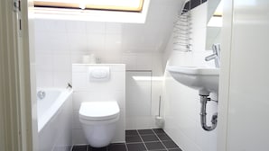 A modern bathroom with a skylight, white tiles, a toilet, a sink, and a bathtub. - Hotel Park Plantage (Amsterdam)