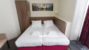 A double bed with white linens and pink footboard, a wooden wardrobe, a cityscape painting on the wall, and a red curtain.